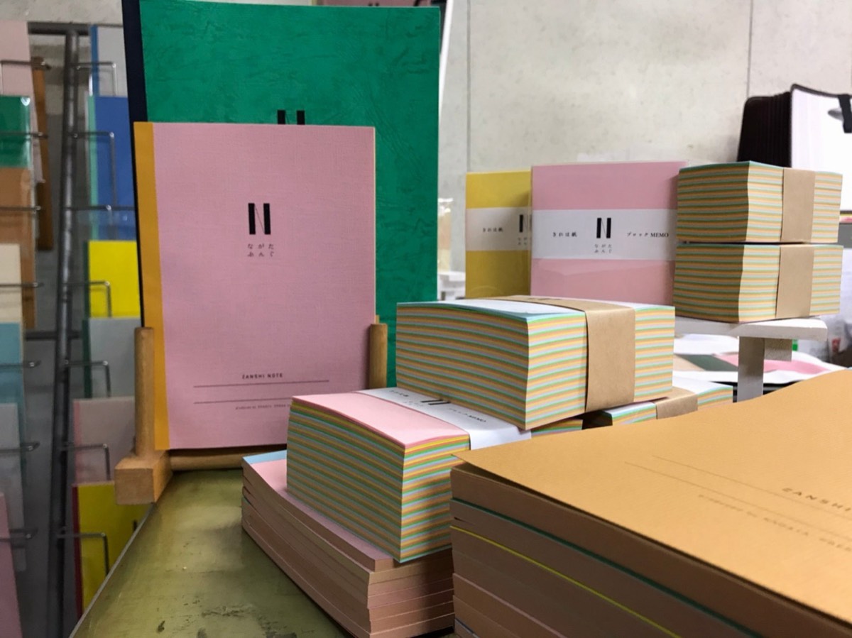 印刷所に並ぶZANSHI NOTEと、色の縞が重なったブロックメモ